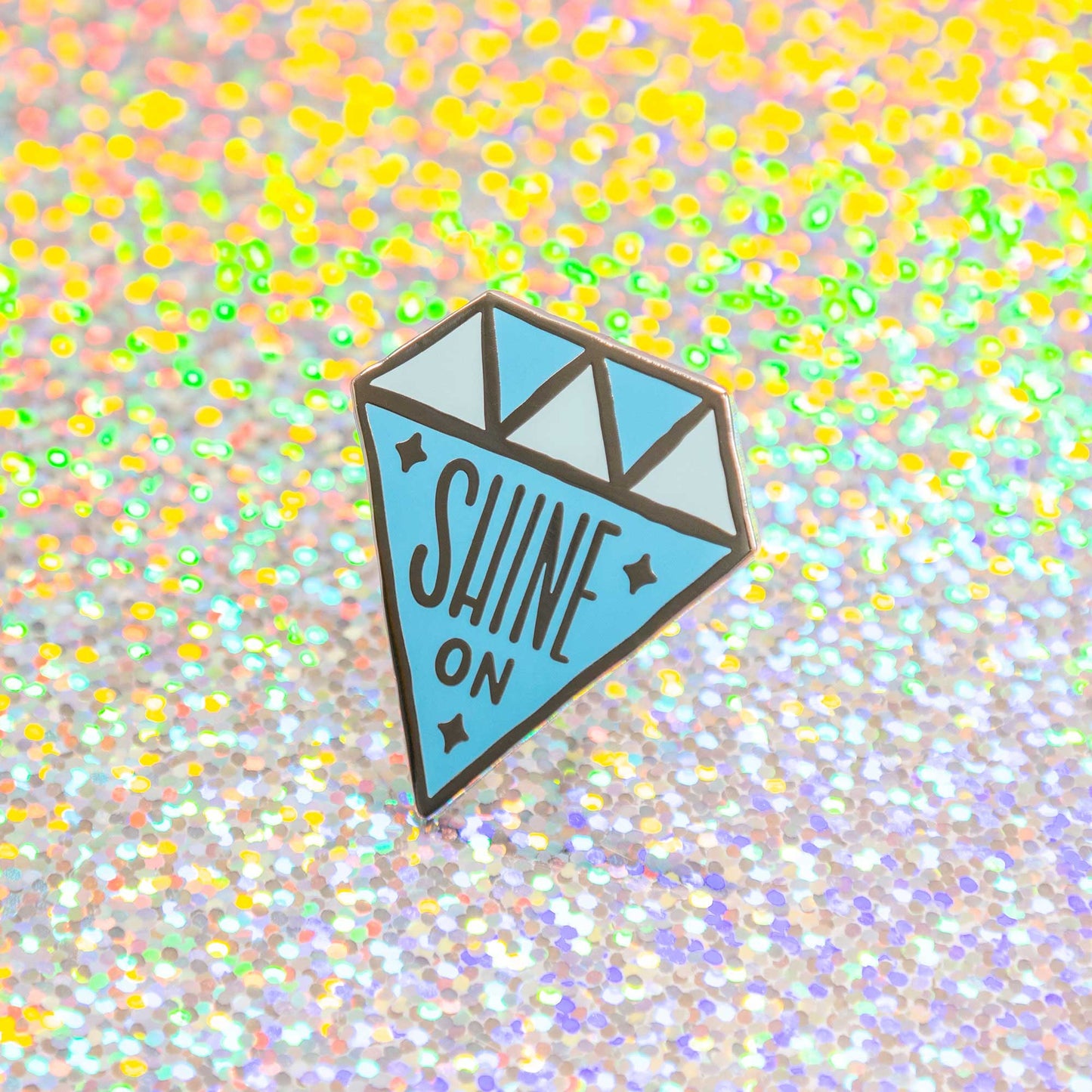 diamond shaped enamel pin that says "shine on"