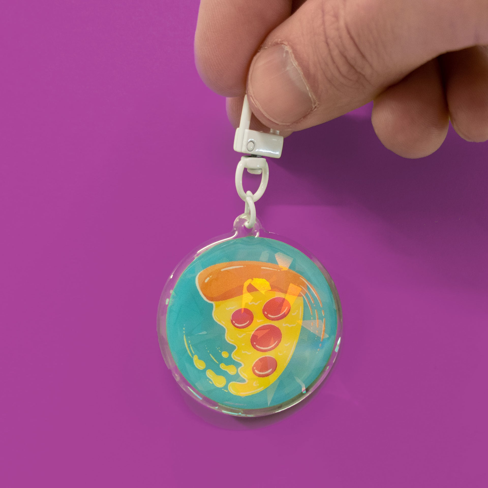 swirling pizza art on a circular holographic keychain in hand