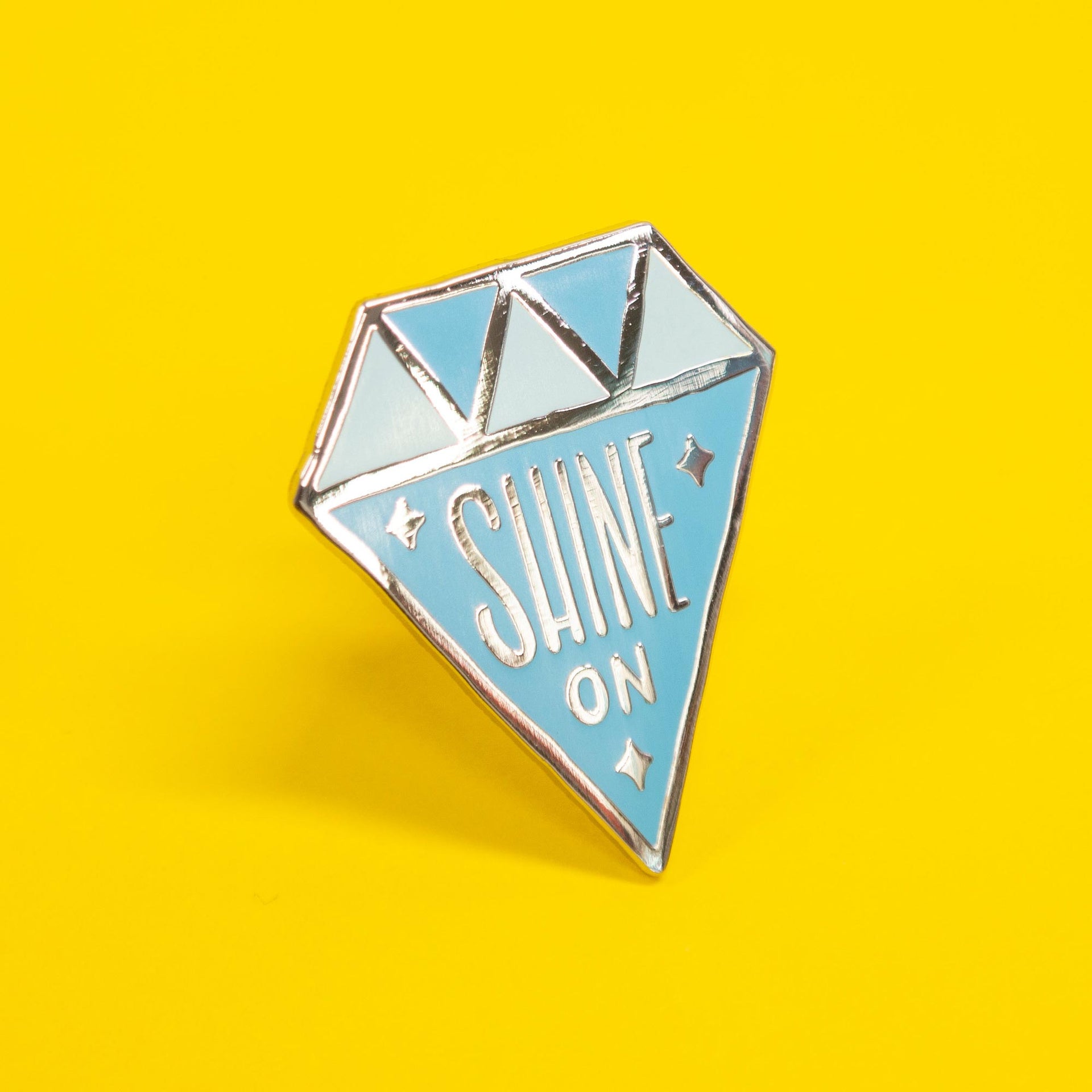 diamond shaped enamel pin that says "shine on"