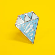 diamond shaped enamel pin that says "shine on"